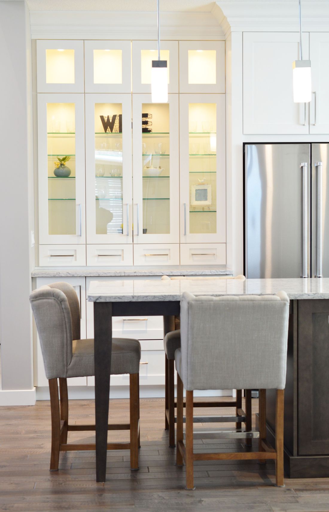 White glass-front built-in cabinet with lighting above a kitchen island