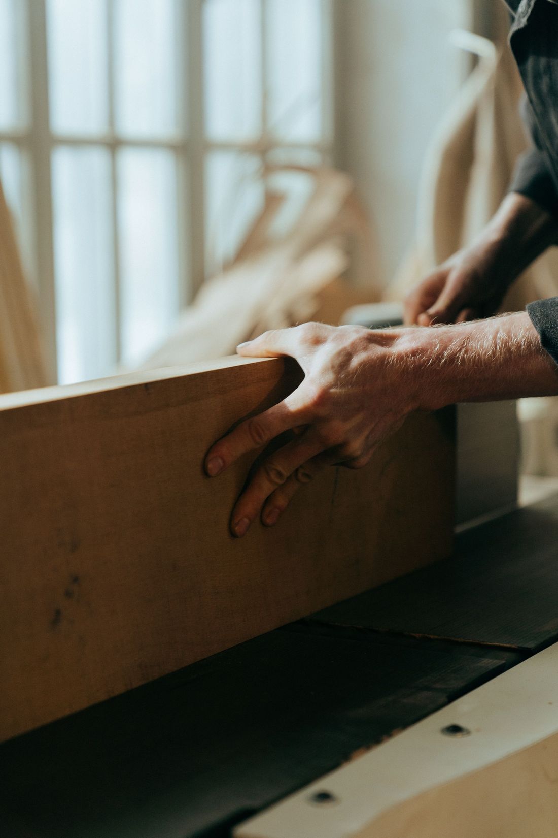 Hands guiding a board through a jointer in a woodworking shop