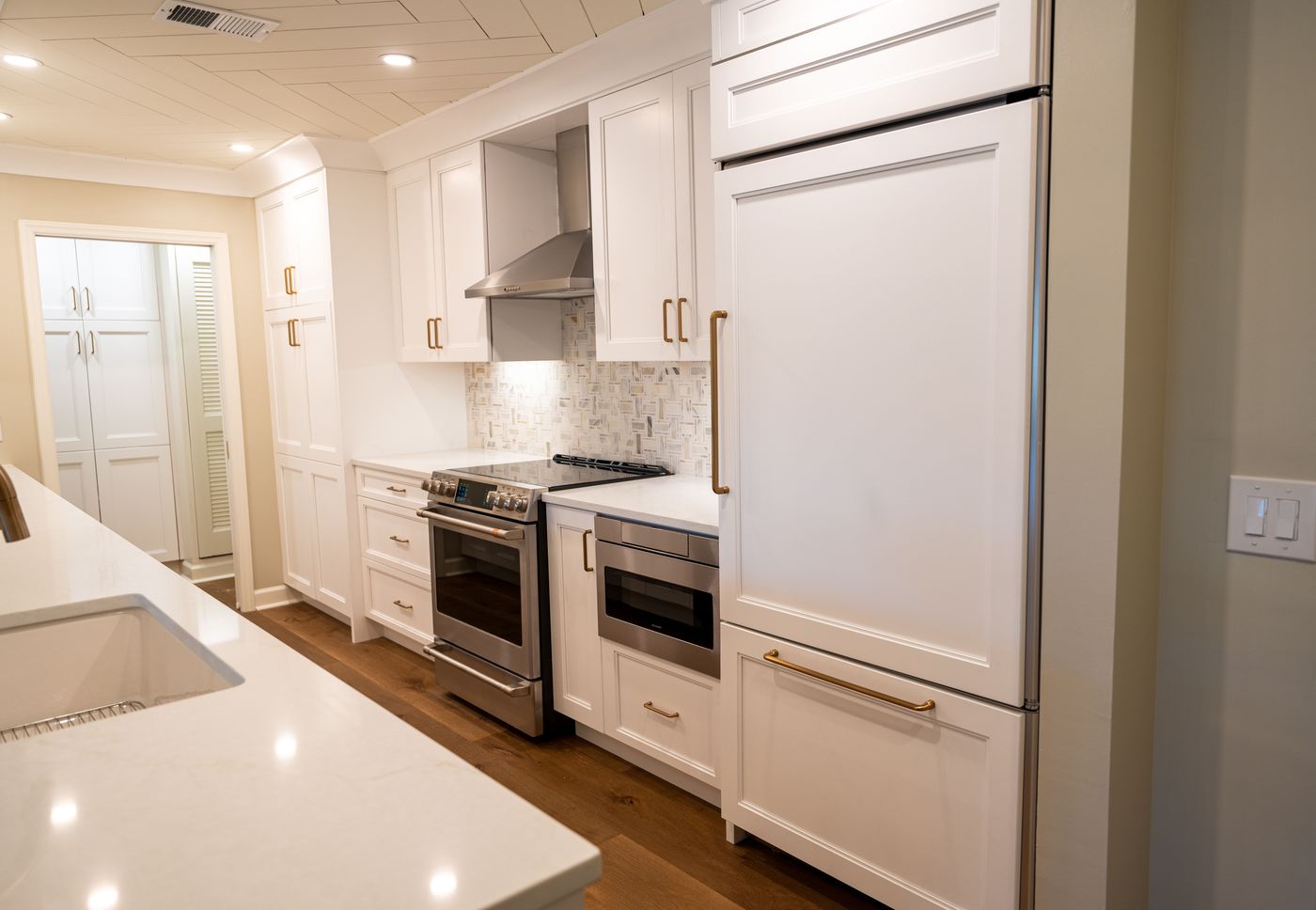 White shaker kitchen cabinets with brass pulls and a paneled refrigerator